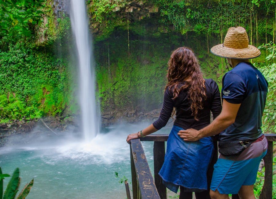 Pareja contemplando una cascada desde un mirador de madera rodeado de exuberante vegetación tropical.